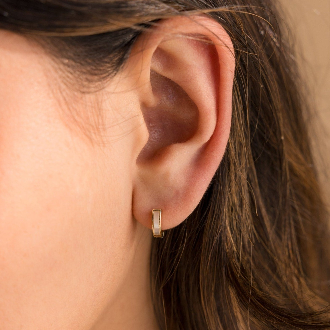 Close-up of a woman's ear wearing Mother of Pearl Inlay Huggies, featuring a small rectangular gold hoop design.