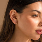 A close-up of a woman’s face, showcasing the elegant Mother of Pearl Inlay Huggies earrings that shimmer beautifully.