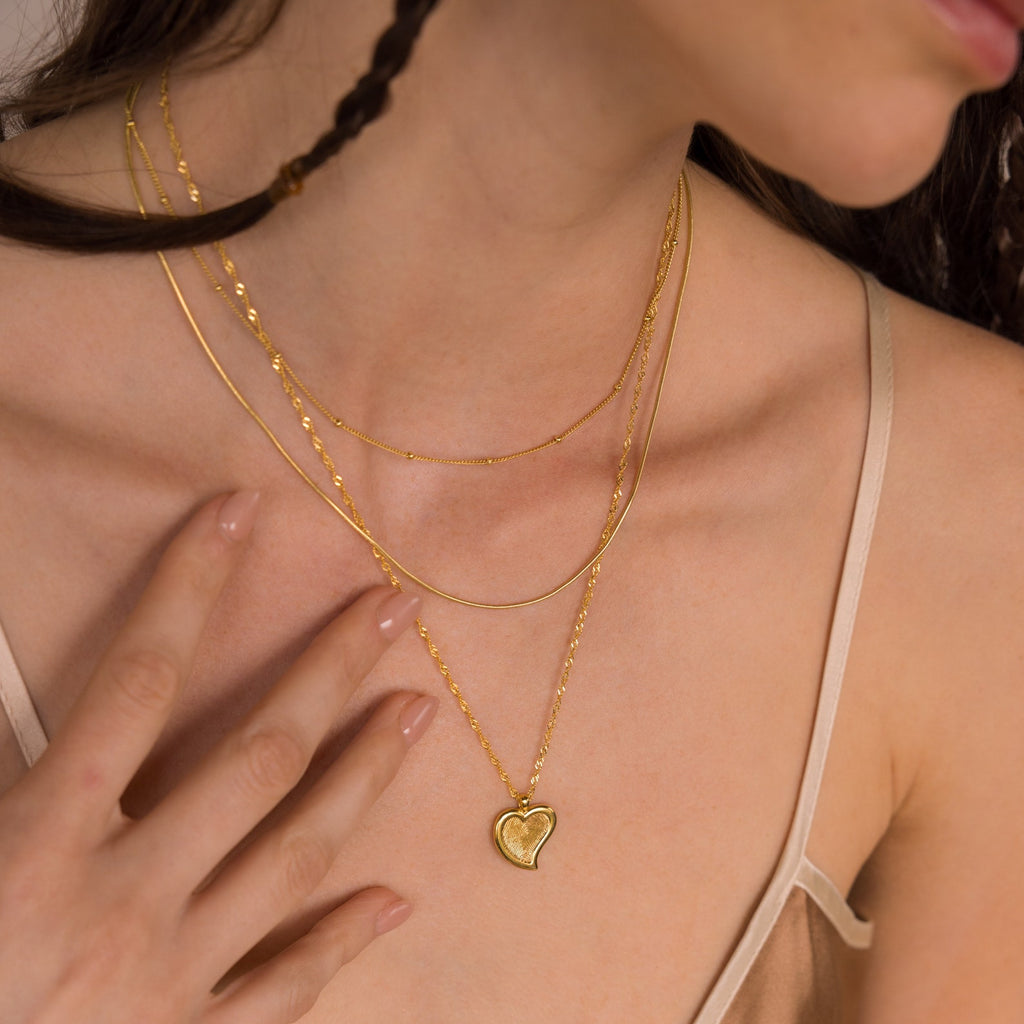 A woman wears a beige camisole and the Fingerprint Heart Necklace, a layered gold piece that makes a meaningful Mother's Day gift.