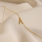 The Mini Pave Sideways Initial Necklace features a gold letter A pendant displayed on soft, cream-colored fabric.