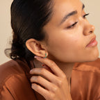 A woman with sleek hair wears elegant Inside Out Emerald Huggies, touching her ear as she gazes thoughtfully to the side.