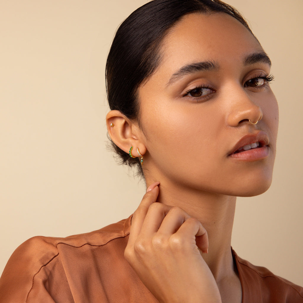 Woman with slicked-back hair touches her earlobe, wearing the Inside Out Emerald Huggies and a brown top.