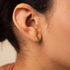 Close-up of a woman's ear wearing the Inside Out Emerald Huggies, small gold hoop earrings with green gemstones, showcasing elegant birthstone jewelry.