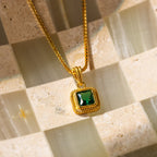 The Vintage Emerald Pendant Necklace features a square emerald gemstone and is displayed on a checkered beige and green stone surface.