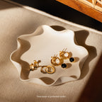 A wavy-edged ceramic dish holds the elegant Mystery Earrings collection, featuring assorted gold hoops and studs, adding charm to a beige surface.