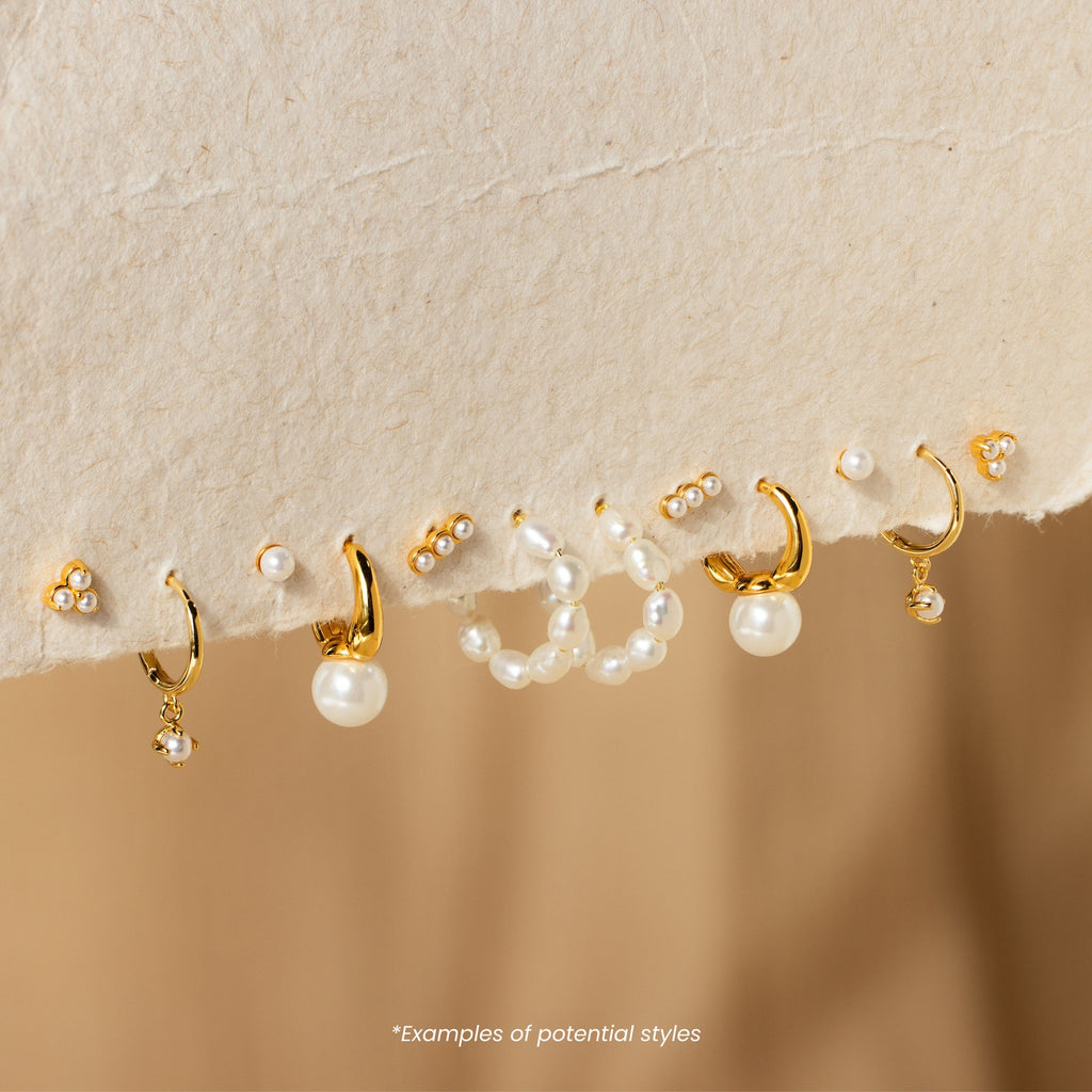 Discover Mystery Earrings—a captivating collection of gold and pearl earrings and studs elegantly displayed on a soft beige surface, perfect for fans who love the thrill of surprise jewelry.