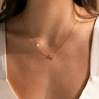 A woman in a white top wears the Mini Pave Sideways Initial Necklace, a delicate gold piece featuring a diamond initial and small airplane pendant.