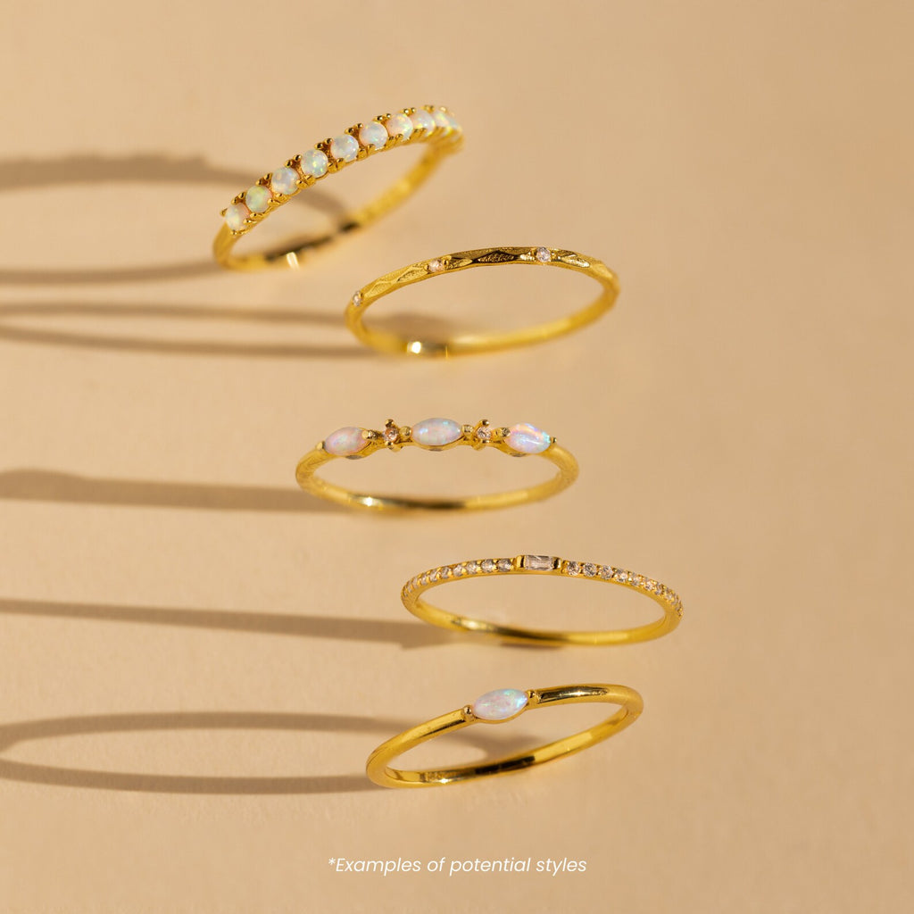 Five Mystery Rings with opal and diamond accents from our eclectic jewelry collection are displayed on a beige background with shadows.