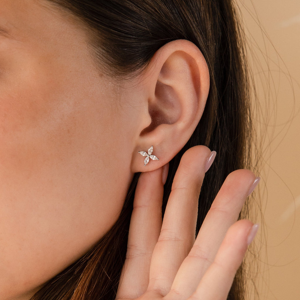 A close-up shows a woman's ear adorned with Marquise Diamond Flower Studs as her hand gently rests near her ear.