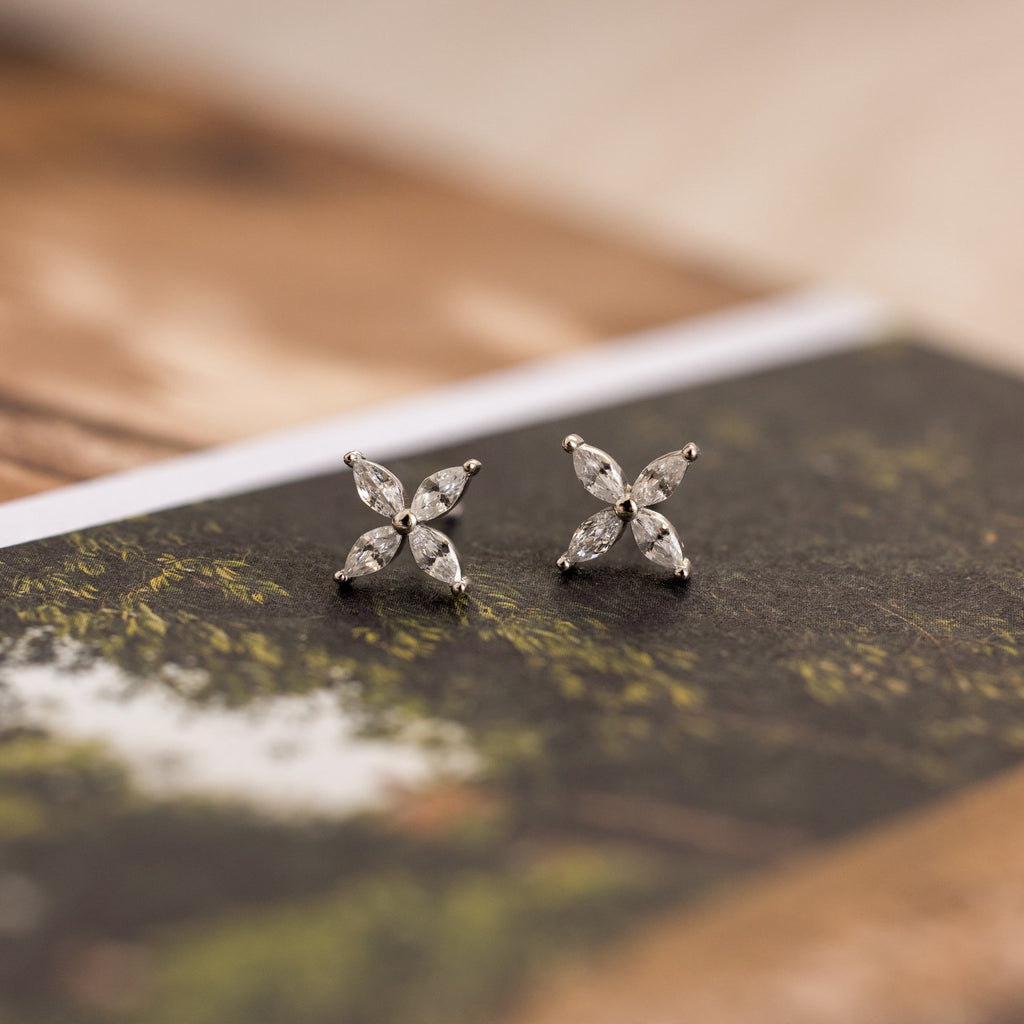 The Marquise Diamond Flower Studs rest on a book, highlighting their elegant floral design—ideal for weddings or any special occasion.