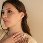 Woman with long brown hair wearing gold jewelry, including the Trio Floral Marquise Studs and rings, looking off to the side.