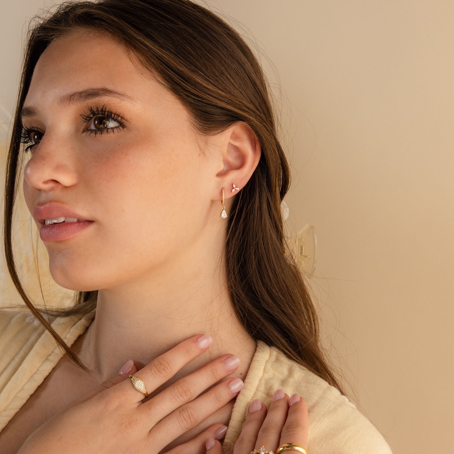 Woman with long brown hair wearing gold jewelry, including the Trio Floral Marquise Studs and rings, looking off to the side.