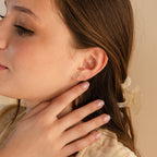 Close-up of a woman touching her ear, wearing the Trio Floral Marquise Studs earring and a light hair clip.