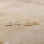 The Trio Floral Marquise Studs set features two pairs of elegant stud earrings in silver and gold, beautifully displayed on a textured beige surface.