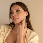 A woman with long brown hair wears the Filigree Flower Ring and a light yellow top, gazing upward with a soft smile.