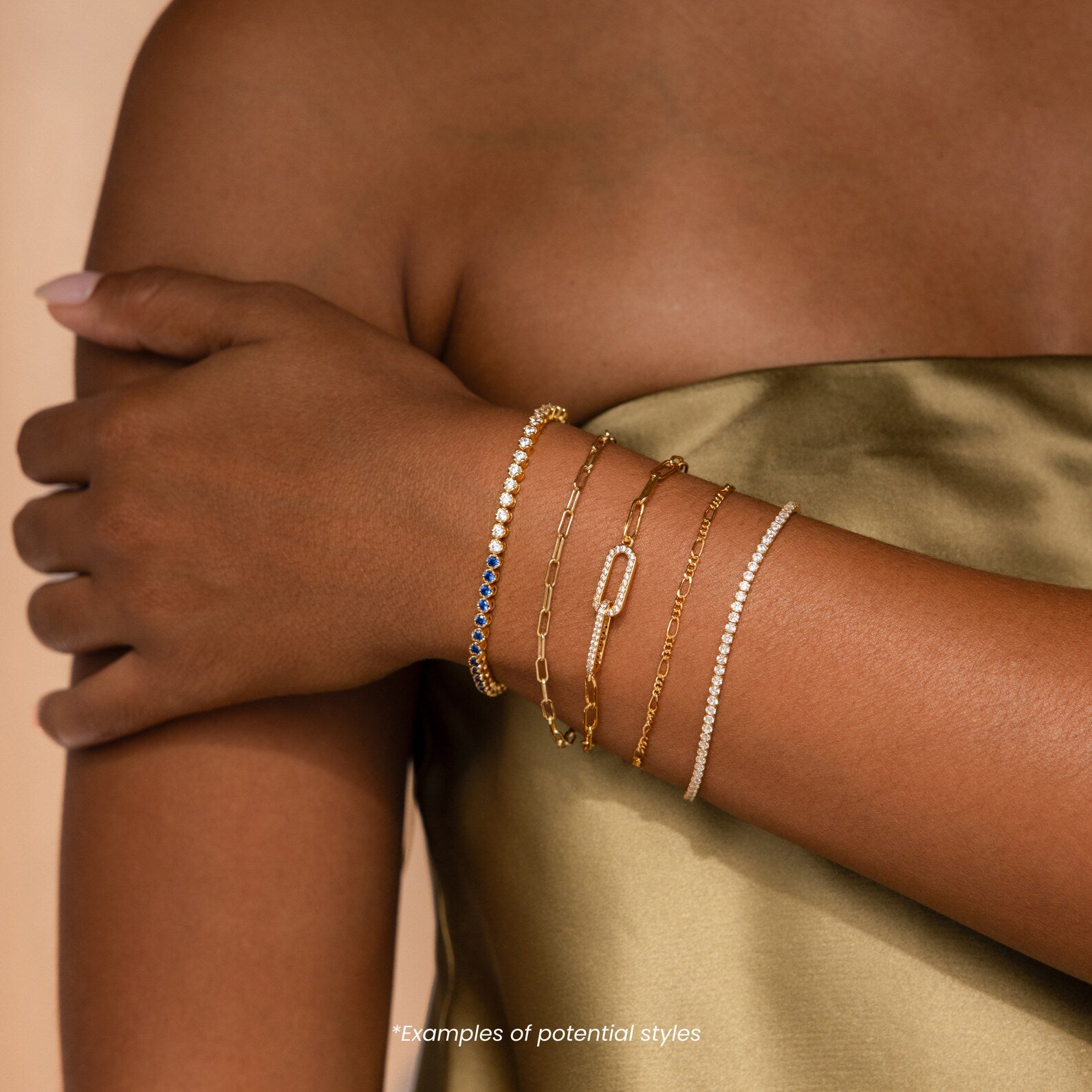 Wearing a satin dress, she radiates sophistication with five shimmering Mystery Bracelets—delicate gold and beaded accents—adorning her arm.
