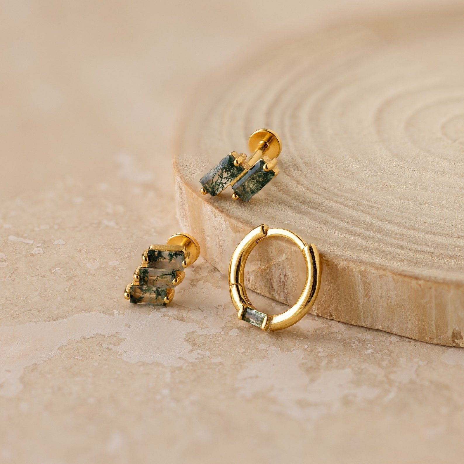 The Agate Cartilage Earrings Set features gold earrings with green stones, displayed elegantly on wood—an ideal gift for best friends and perfect for cartilage piercings.