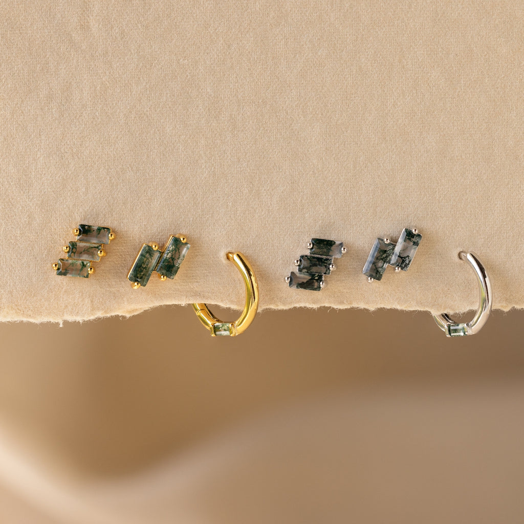 The Agate Cartilage Earrings Set features four mismatched earrings with green gemstones—two gold and two silver—perfect for a unique gift for best friends, displayed on a textured beige surface.