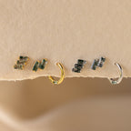 The Agate Cartilage Earrings Set features four mismatched earrings with green gemstones—two gold and two silver—perfect for a unique gift for best friends, displayed on a textured beige surface.