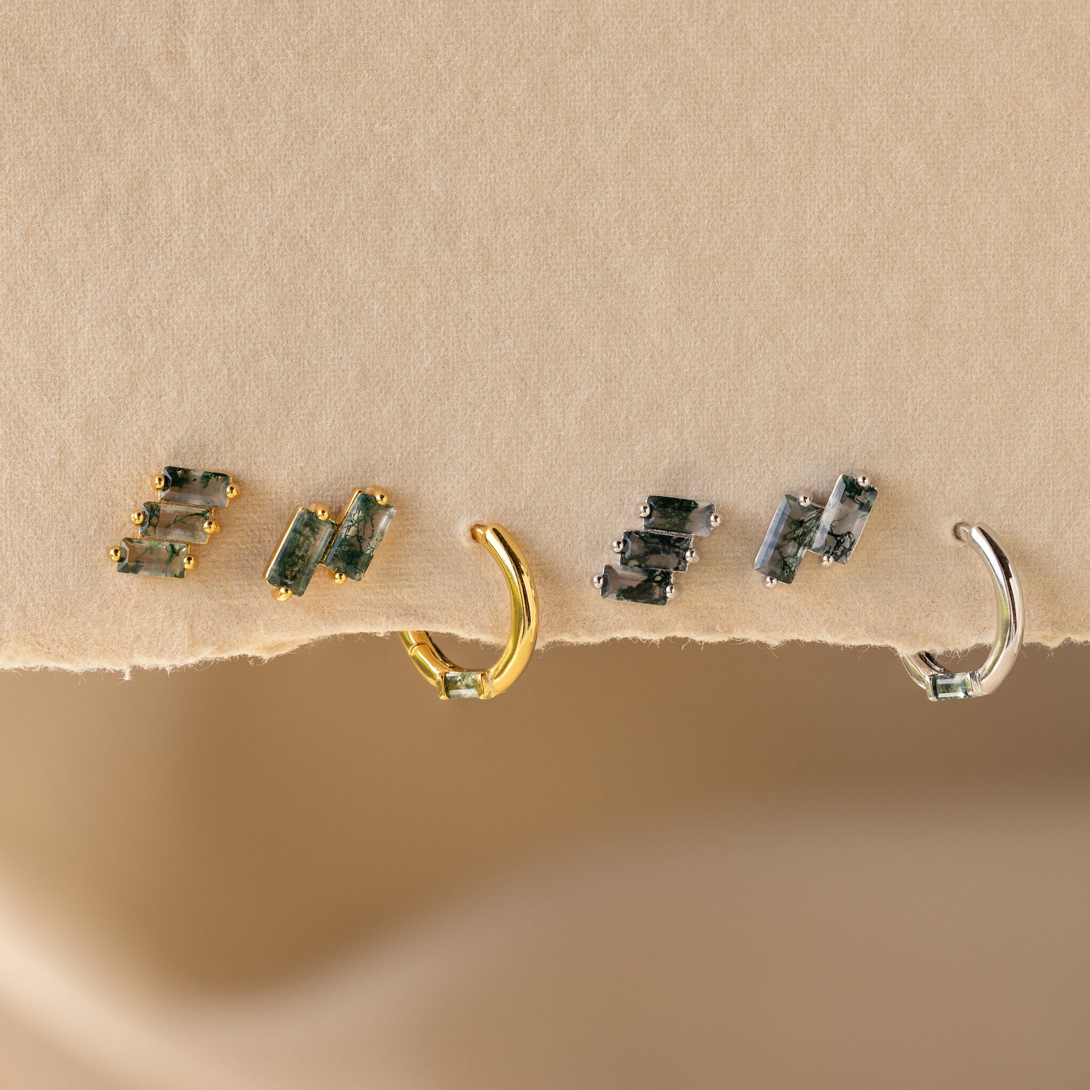 The Agate Cartilage Earrings Set features four mismatched earrings with green gemstones—two gold and two silver—perfect for a unique gift for best friends, displayed on a textured beige surface.