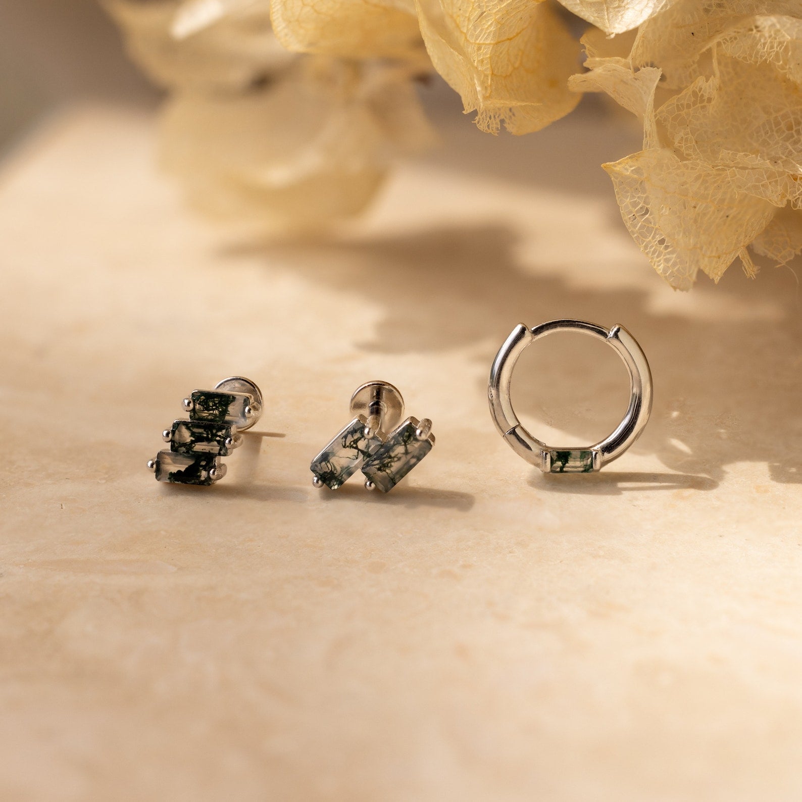 The Agate Cartilage Earrings Set features three silver earrings with green gemstones, displayed on beige with dried flowers—an ideal gift for best friends or a stylish choice for cartilage piercings.