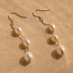 Close-up of a pair of long silver pearl chain earrings set against a tan background.
