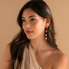 Model wearing long pearl dangle earrings, diamond tennis chain earrings, and diamond stud earrings in gold.