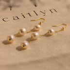 Close-up of long gold pearl chain earrings on beige fabric.