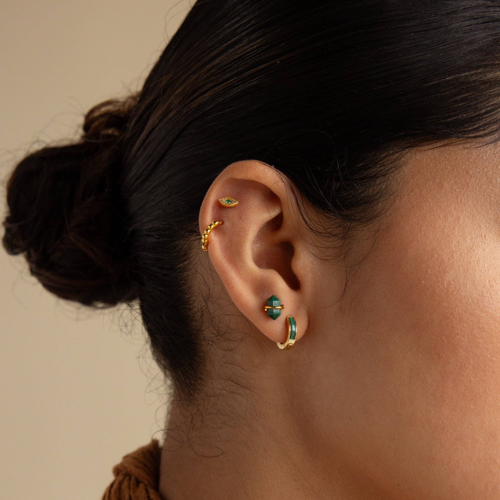 A close-up of a woman's ear with her hair in a bun, featuring the Herkimer Malachite Studs in gold and green malachite.