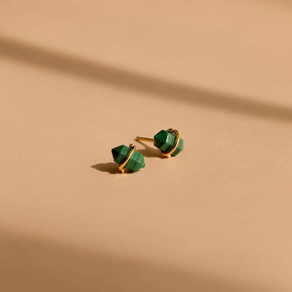 Herkimer Malachite Studs feature gold geometric design with green stone accents, displayed on a beige surface with soft shadows.