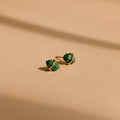 Herkimer Malachite Studs feature gold geometric design with green stone accents, displayed on a beige surface with soft shadows.