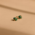 Herkimer Malachite Studs feature gold geometric design with green stone accents, displayed on a beige surface with soft shadows.