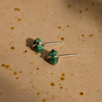 Two green Herkimer Malachite Studs with silver posts sit on a beige, speckled surface, highlighting their modern geometric gemstone earring style.