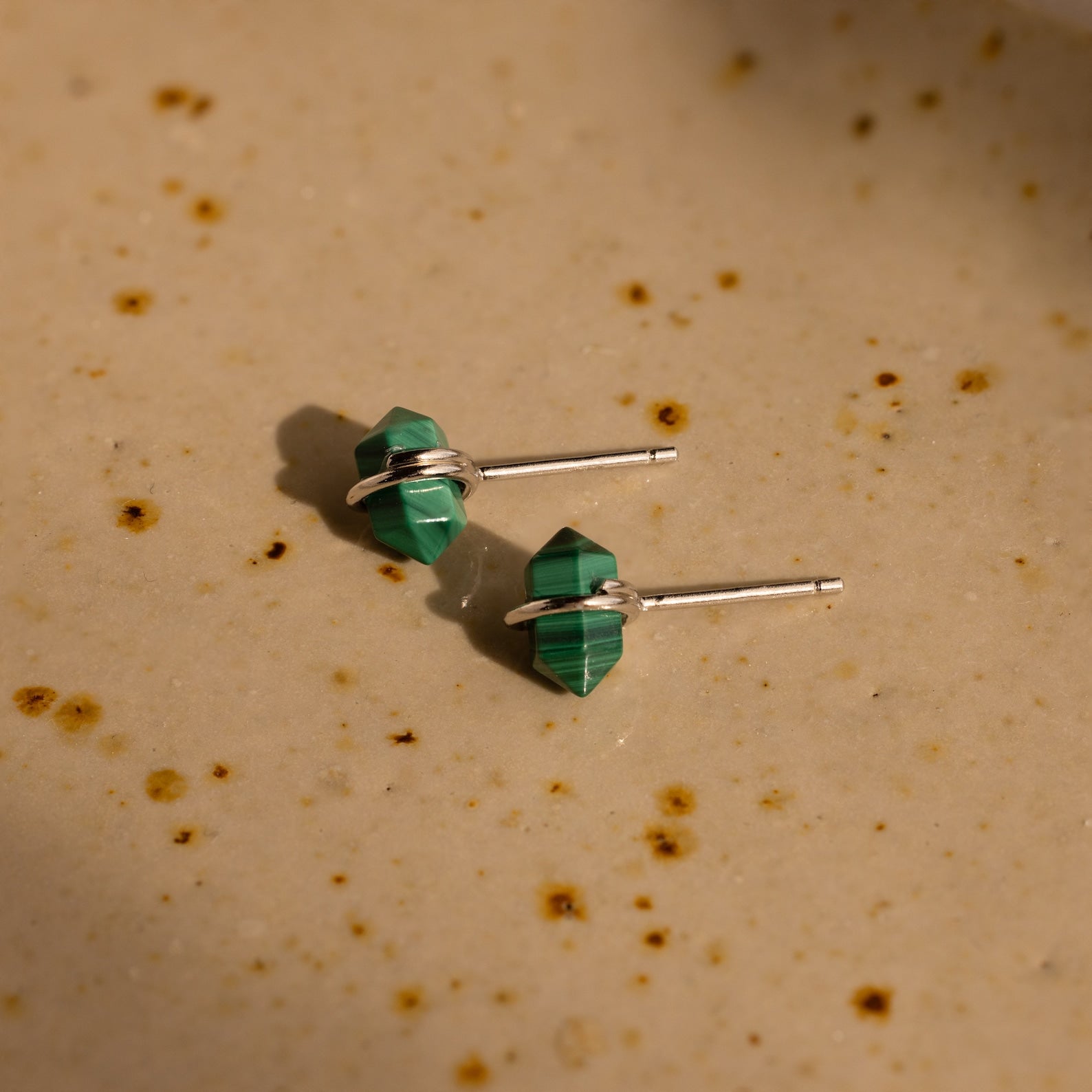 Two green Herkimer Malachite Studs with silver posts sit on a beige, speckled surface, highlighting their modern geometric gemstone earring style.
