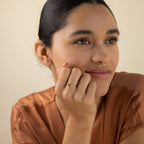 A woman with dark hair and a gold nose ring smiles in a brown top, resting her chin on her hand and subtly showcasing the Agate Baguette Ring as it catches the light.