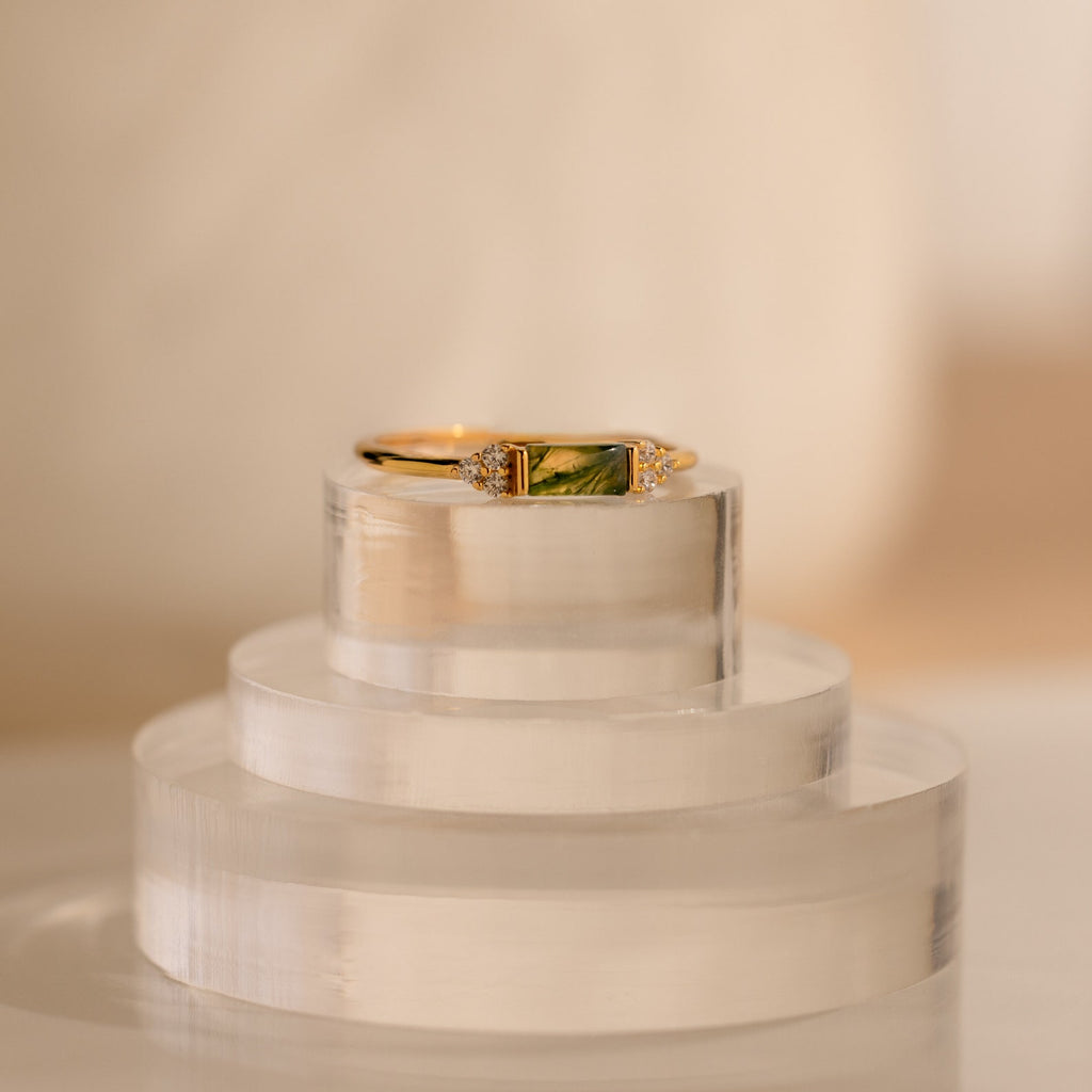 Agate Baguette Ring featuring a green rectangular stone and sparkling diamond accents, displayed on a clear, layered stand.