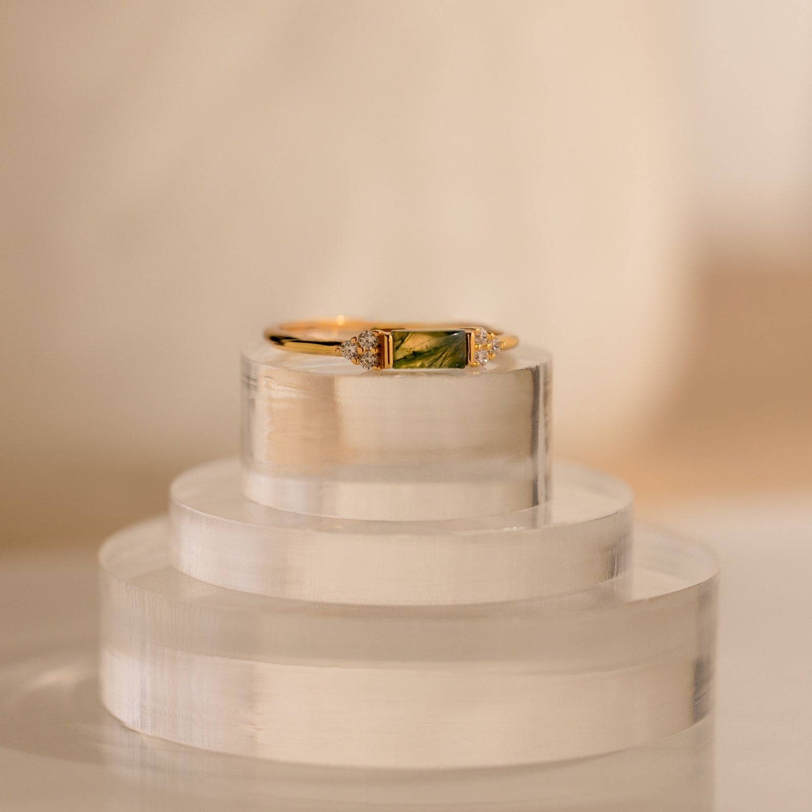 Agate Baguette Ring featuring a green rectangular stone and sparkling diamond accents, displayed on a clear, layered stand.
