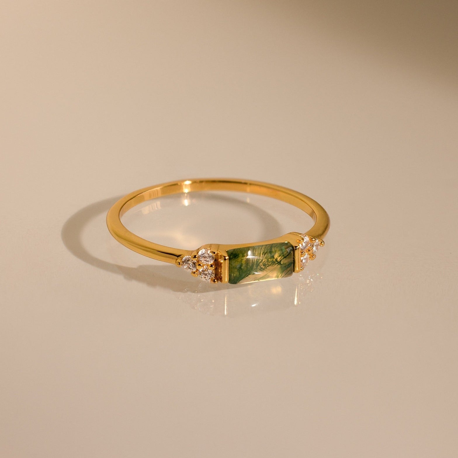 The Agate Baguette Ring showcases a rectangular green gemstone with sparkling diamonds on each side, all set in gold and photographed on a neutral background.