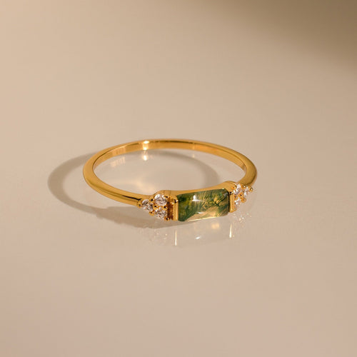 The Agate Baguette Ring showcases a rectangular green gemstone with sparkling diamonds on each side, all set in gold and photographed on a neutral background.