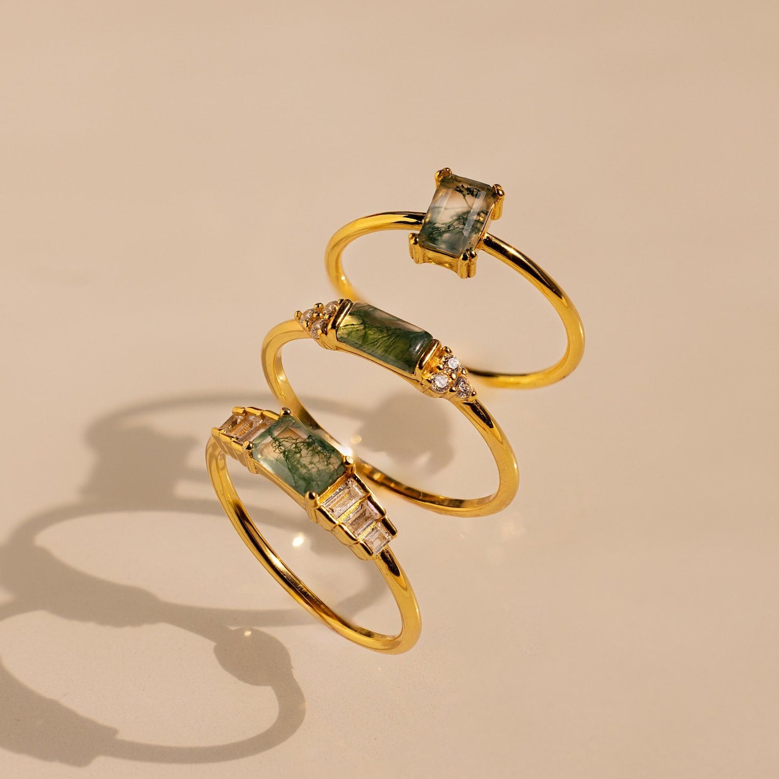 Three Agate Baguette Rings with rectangular green agate and sparkling diamonds are beautifully displayed on a light beige background.