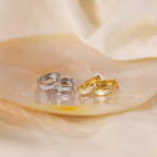 Two pairs of Mother of Pearl Inlay Huggies, one in silver and one in gold, are elegantly displayed on a shiny oval dish with a soft background.
