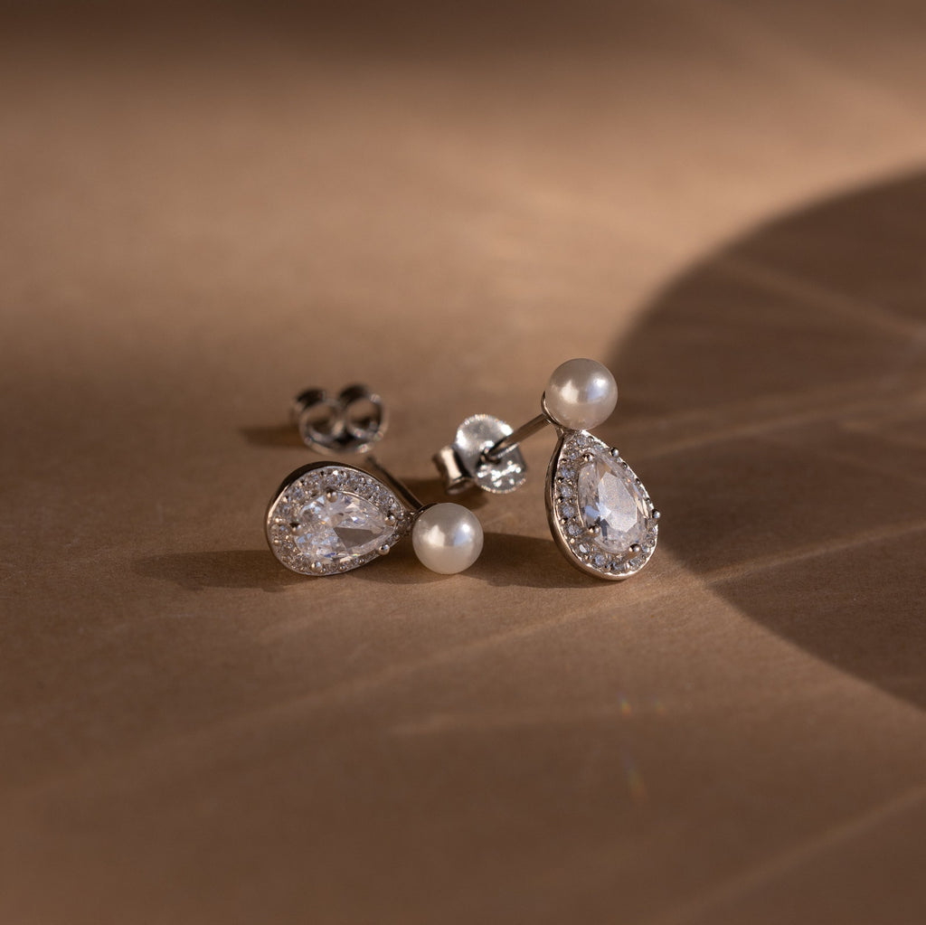 The Pearl Diamond Teardrop Studs rest on a softly lit brown surface.