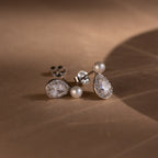 The Pearl Diamond Teardrop Studs rest on a softly lit brown surface.
