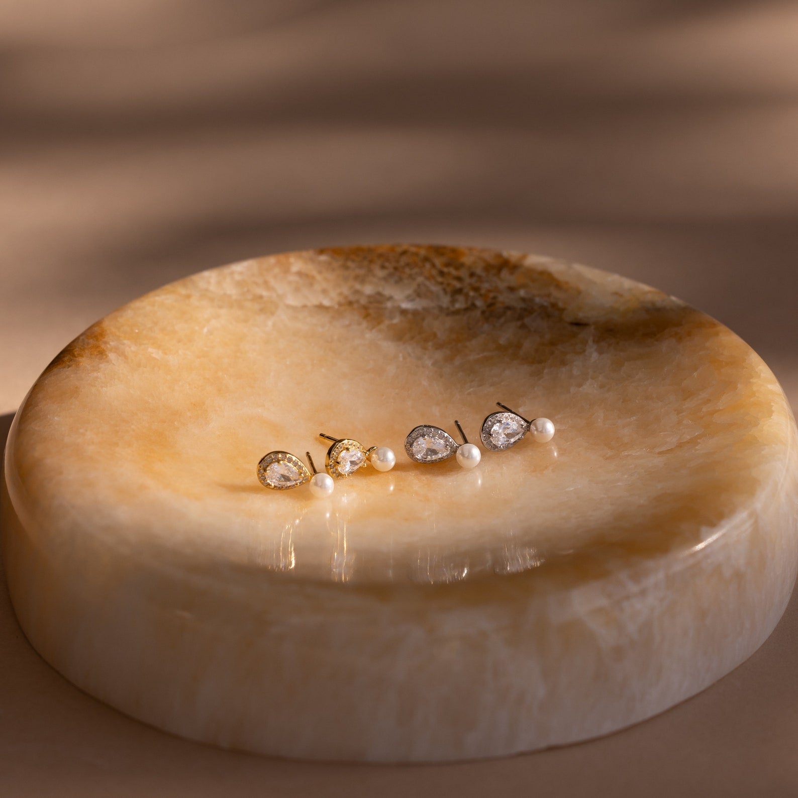 Pearl Diamond Teardrop Studs showcased on a round, polished beige stone dish under gentle lighting.