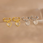 Two pairs of Diamond Heart Drop Huggies—coquette-inspired heart-shaped earrings in gold and silver, each with a clear gemstone at the center—add charming sparkle to any look.