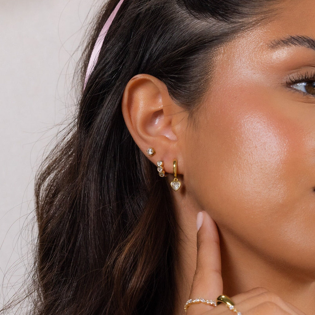 Close-up of a woman's ear wearing Diamond Bezel Heart Huggies as she gently touches her earlobe.