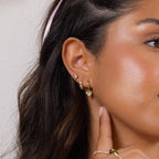 Close-up of a woman's ear wearing Diamond Bezel Heart Huggies as she gently touches her earlobe.