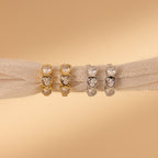 Four heart-shaped gemstone rings in gold and silver rest on beige fabric, beautifully complemented by our Diamond Bezel Heart Huggies for a romantic touch.