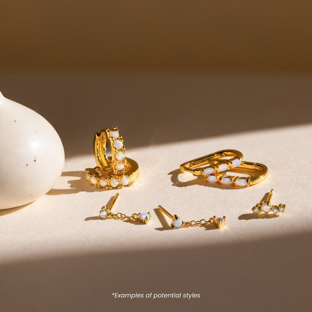 Mystery Earrings from our collection, featuring gold and opal designs in various styles, are displayed on a light surface beside a white vase.