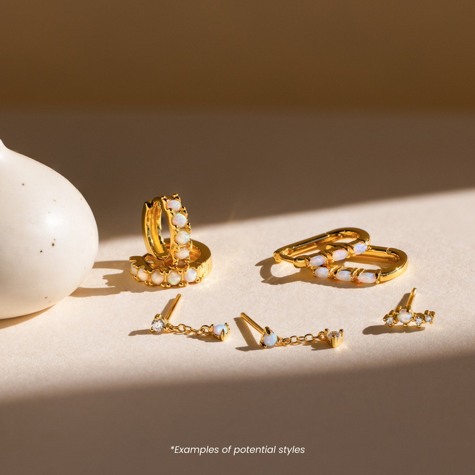 Mystery Earrings from our collection, featuring gold and opal designs in various styles, are displayed on a light surface beside a white vase.